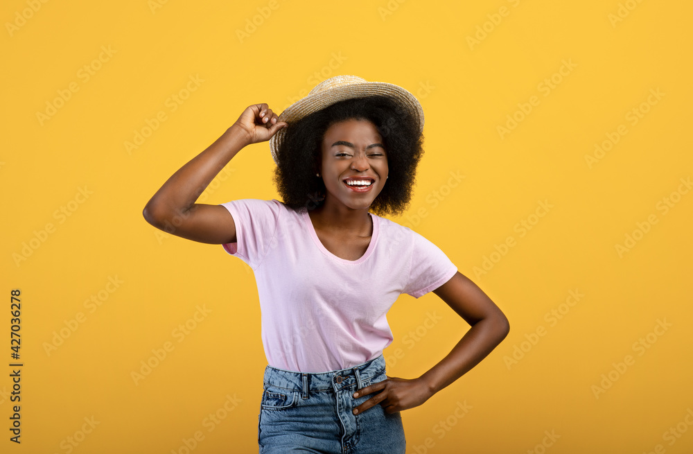 Happy black woman in straw hat posing on yellow studio background, smiling and looking at camera Happy black woman in straw hat posing on yellow studio background, smiling and looking at camera
