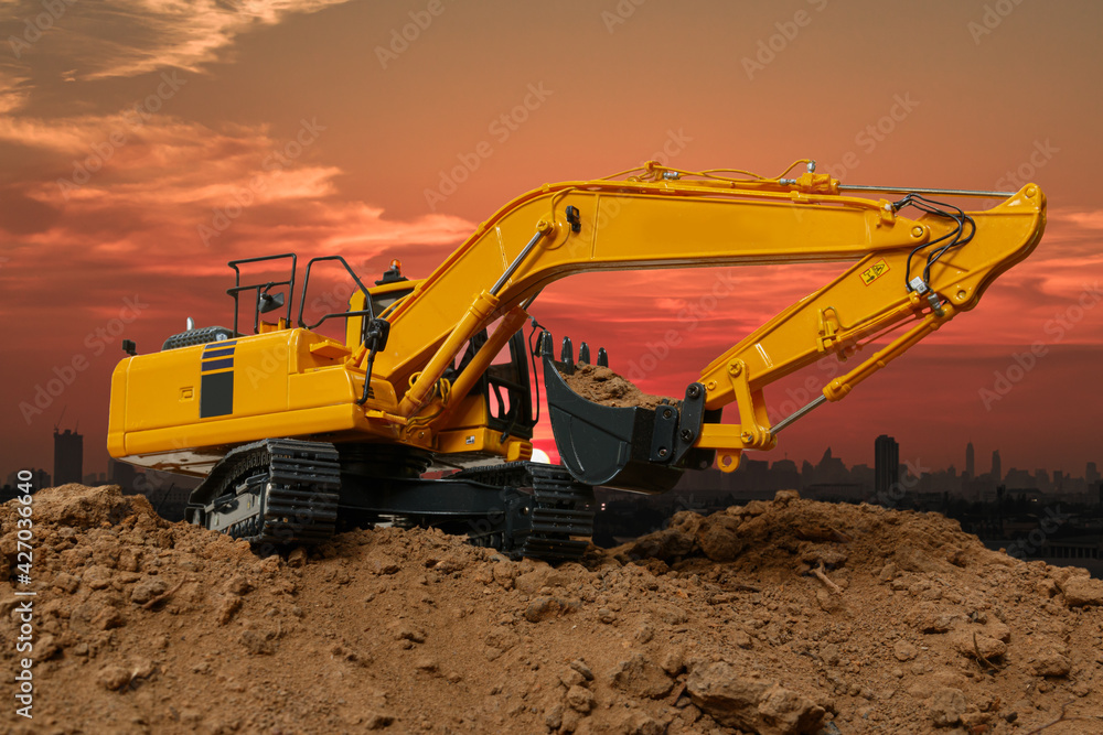 Excavators are digging the soil in the construction site on the sunset sky background Excavators are digging the soil in the construction site on the sunset sky background
