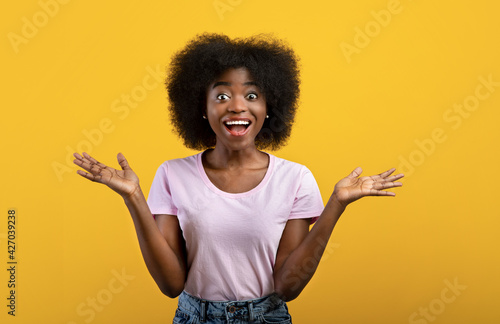 Omg. Overjoyed african american lady shouting in excitement and looking at camera, posing over yellow studio background photo