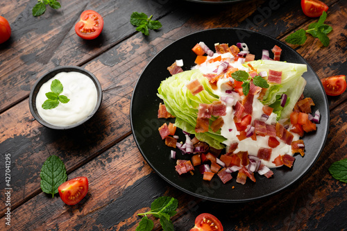 Iceberg wedge salad with bacon, cherry tomatoes, red onion and dressing. healthy food