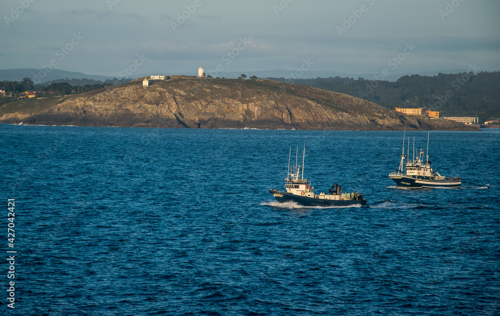 Dos barcos pesqueros salen de la bahía al atardecer para ir a faenar durante la noche, en una localidad del norte de España