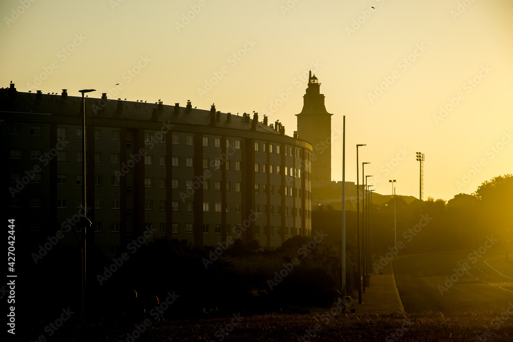 Puesta de sol que sólo permite entrever un edificio de apartamentos y la silueta de la Torre de Hércules, el faro romano más antiguo y mejor conservado del mundo en la ciudad de La Coruña, España
