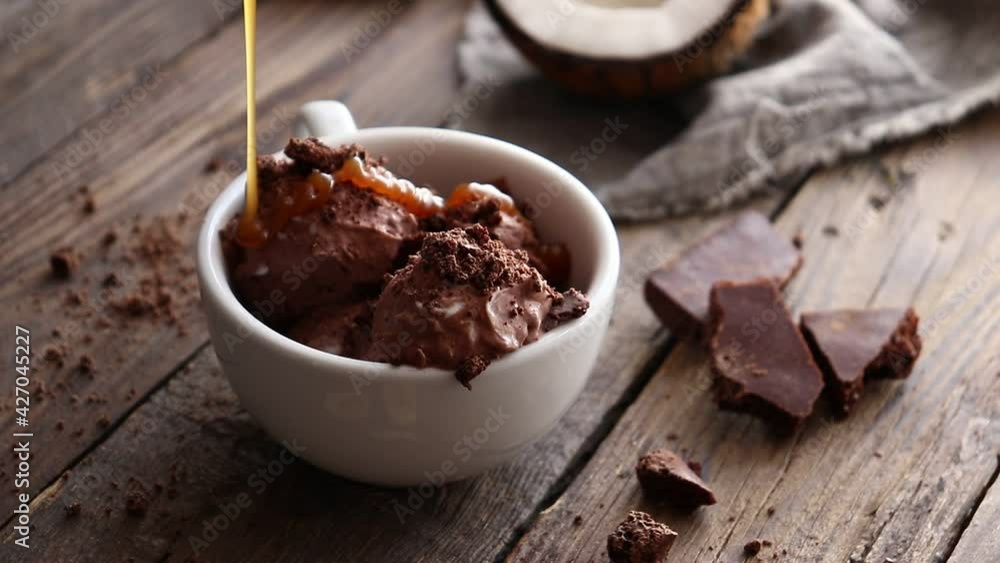 Chocolate ice cream poured over with caramel. Wooden background. Dessert in a cafe. Coconut vegan ice cream. Chocolate ice cream poured over with caramel. Wooden background. Dessert in a cafe. Coconut vegan ice cream.