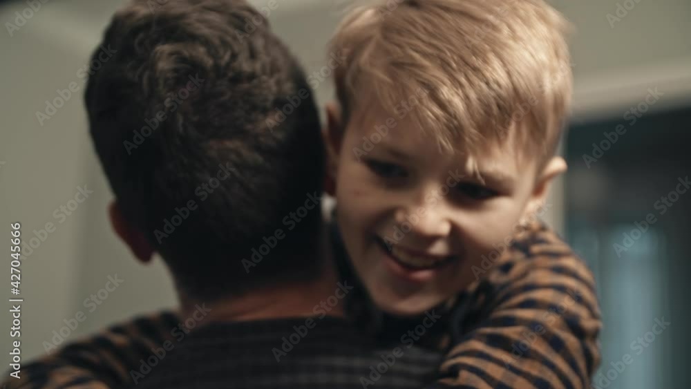 Smiling son meeting his dad at the door in the evening. Concept of joy. Close-up of happy teenage son in casual clothes runnig to his father and hugging him. Young dad finally coming home from work. Smiling son meeting his dad at the door in the evening. Concept of joy. Close-up of happy teenage son in casual clothes runnig to his father and hugging him. Young dad finally coming home from work.