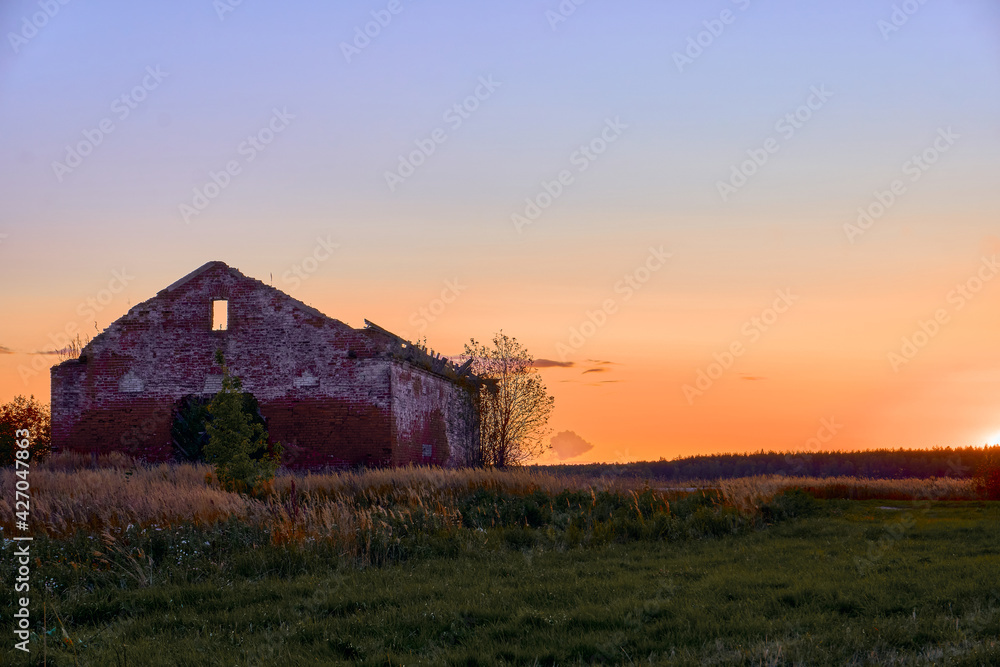 At sunset in the field stands a destroyed building, an old building, a blue sky with the transition of a yellow sunset. A field with green grass and thumping shods. Abandoned building. At sunset in the field stands a destroyed building, an old building, a blue sky with the transition of a yellow sunset. A field with green grass and thumping shods. Abandoned building.