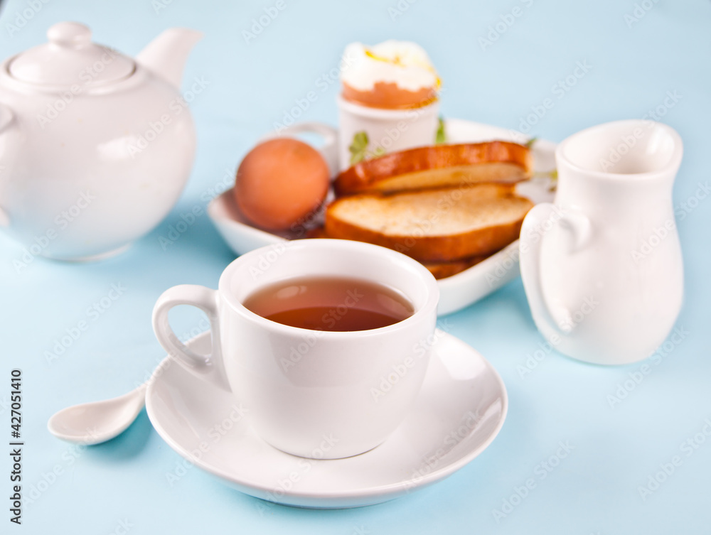 Cup of tea and boiled egg in eggcup on wooden board with crispy toast. Breakfast concept. Cup of tea and boiled egg in eggcup on wooden board with crispy toast. Breakfast concept.