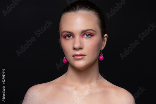 High beauty photo of sexy young girl with blue eyes, round pink earrings and wonderful professional makeup
