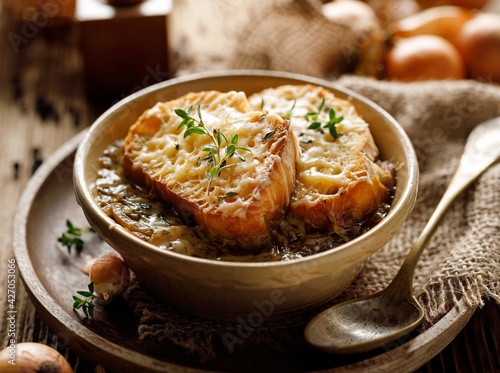 Classic French onion soup baked with cheese croutons sprinkled with fresh thyme, close up view.