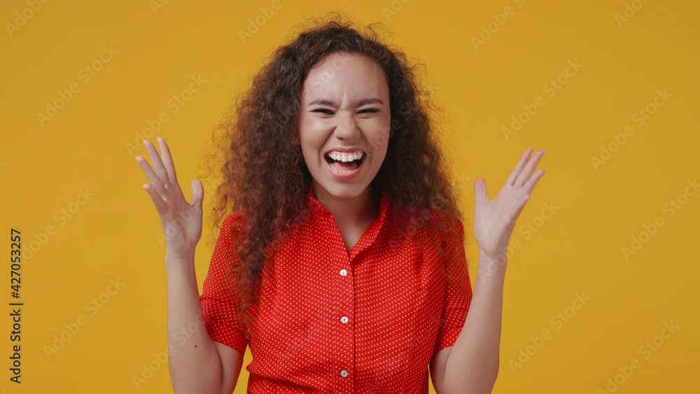 Shocked joyful young african american woman 20s in red dotted shirt posing isolated on yellow background studio. People lifestyle concept. Doing winner gesture celebrating clenching fists say yes Shocked joyful young african american woman 20s in red dotted shirt posing isolated on yellow background studio. People lifestyle concept. Doing winner gesture celebrating clenching fists say yes