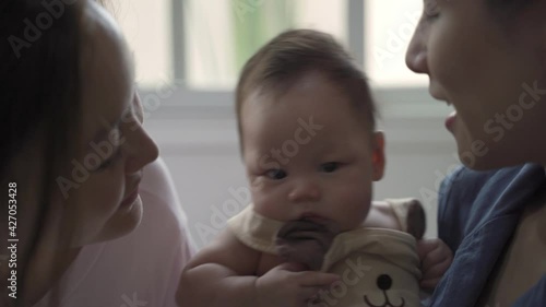 Authentic shot of young happy asian homosexual female gay family with baby infant in living room. LGBT and LGBTQ baby adoption concepts. woman mother parent kissing innocence kid. life at home.