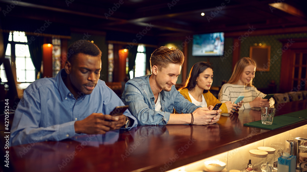 Friends using mobile phones at the counter in bar Friends using mobile phones at the counter in bar