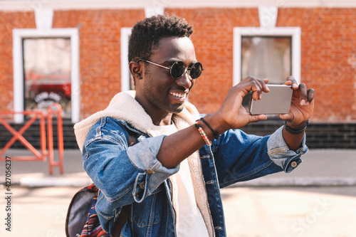 Portrait of happy smiling young african american man taking selfie by smartphone on a city street