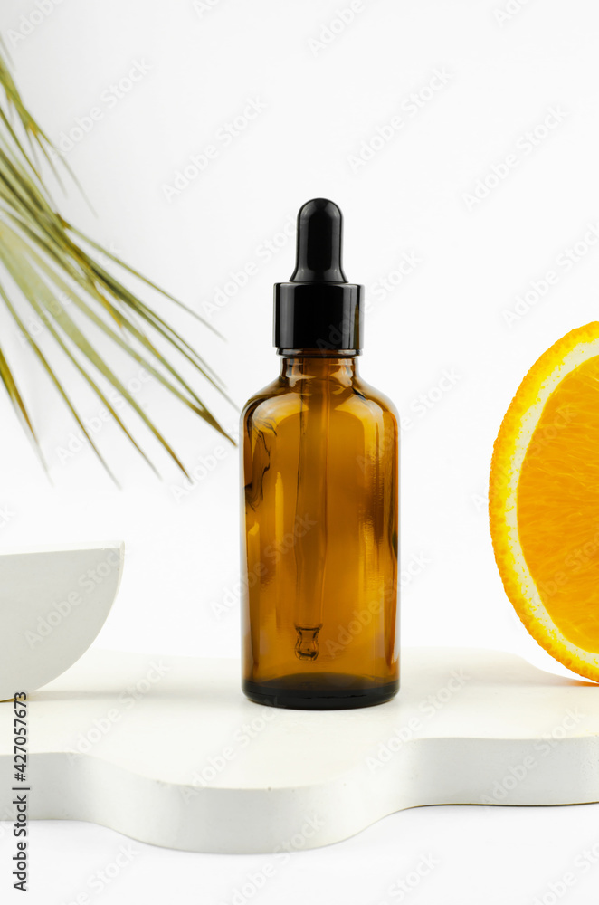 Serum in a glass bottle with a pipette. Natural essential oil on a white podium. Packaging for a cosmetic product. Oils with orange extract Serum in a glass bottle with a pipette. Natural essential oil on a white podium. Packaging for a cosmetic product. Oils with orange extract
