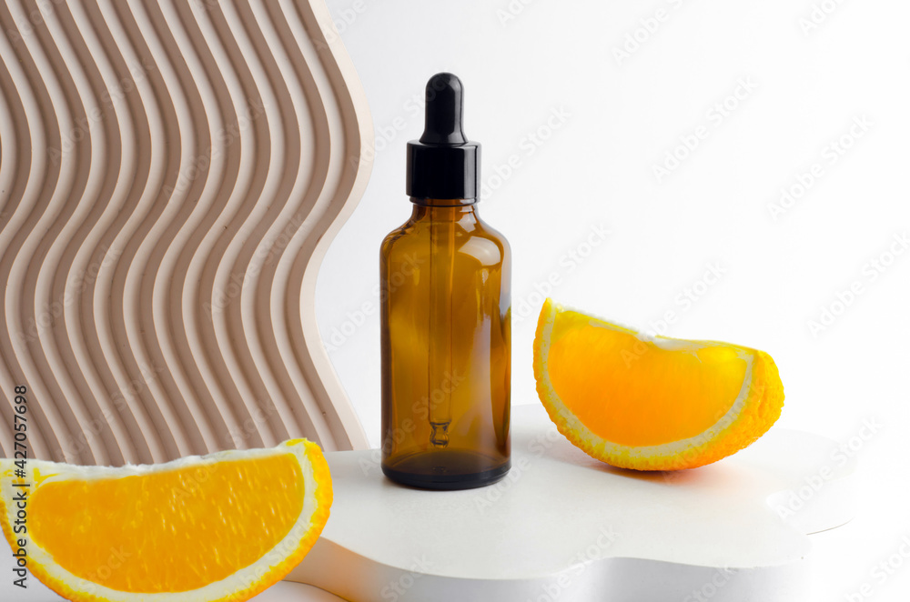 Serum in a glass bottle with a pipette. Natural essential oil on a white podium. Packaging for a cosmetic product. Oils with orange extract Serum in a glass bottle with a pipette. Natural essential oil on a white podium. Packaging for a cosmetic product. Oils with orange extract