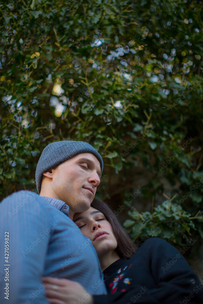 A young couple guy and a girl hug each other standing with their eyes closed against a bright green tree. Love story. Feelings. High quality photo A young couple guy and a girl hug each other standing with their eyes closed against a bright green tree. Love story. Feelings. High quality photo