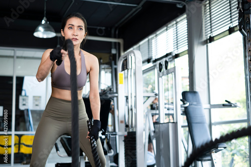 Young Asian girl in fitness gym. Asian woman working out in gym doing strength training working out with battle rope. Fitness woman exercising indoor in fitness center. Female with in gym.