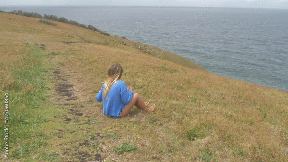 Girl Sitting On Grass While Enjoying Canned Drink And Feeling Cold Ocean Breeze At Crescent Head Lookout - Big Nobby Peninsula In NSW, Australia. - wide shot Girl Sitting On Grass While Enjoying Canned Drink And Feeling Cold Ocean Breeze At Crescent Head Lookout - Big Nobby Peninsula In NSW, Australia. - wide shot