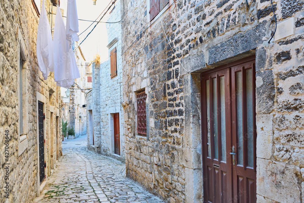 Narrow pavements in one of the old towns on the Adriatic coast, shiny cobblestones and tall tenement houses, drying clothes in the background
