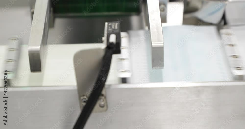 3-Ply Surgical Face Mask Coming Out Of Machine To Ear Loop Attaching. close up, panning right 3-Ply Surgical Face Mask Coming Out Of Machine To Ear Loop Attaching. close up, panning right