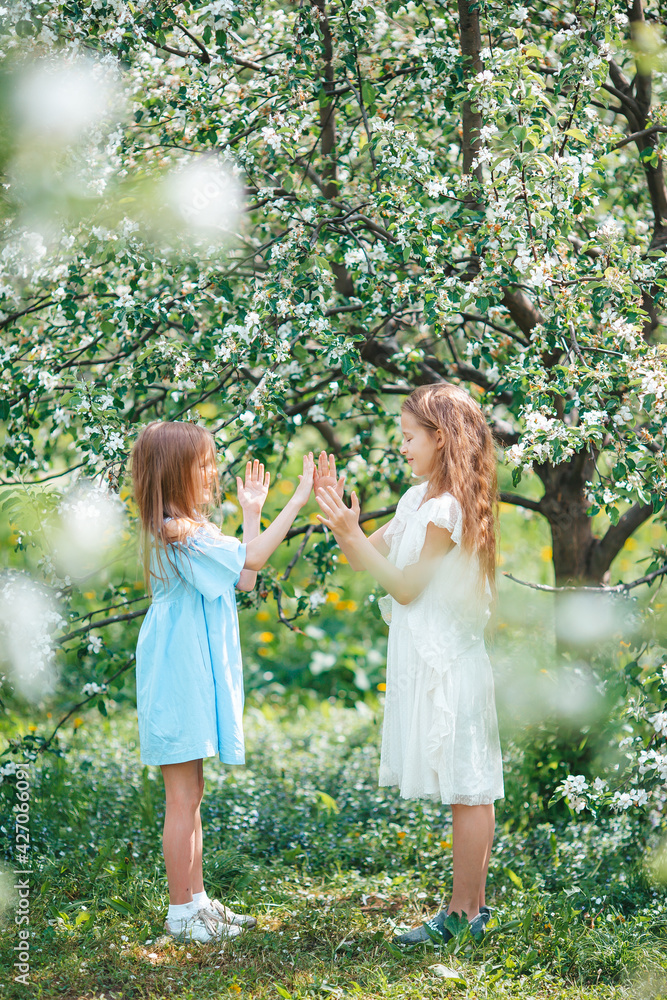 Adorable little girls in blooming apple tree garden on spring day Adorable little girls in blooming apple tree garden on spring day