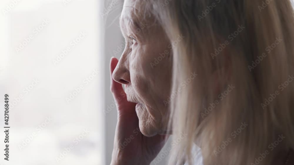 Old lonely woman suffering from headache. Looking through the window. High quality 4k footage Old lonely woman suffering from headache. Looking through the window. High quality 4k footage