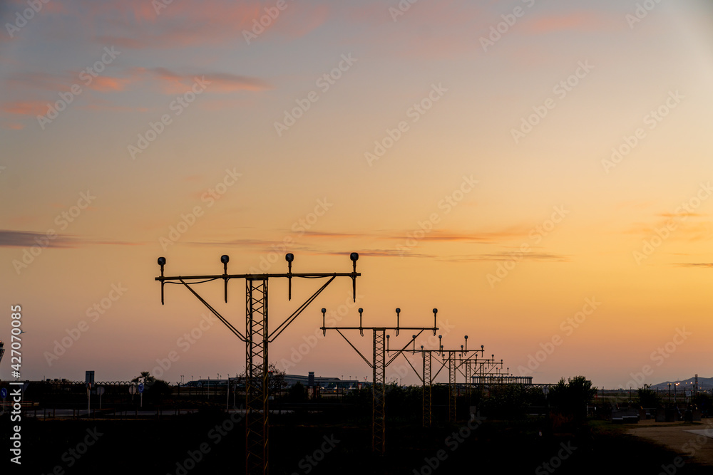 Fototapeta premium Silhouette of runway signs during sunset. In the sky we can see red clouds as if they were fire. We can also see the control tower in the background.