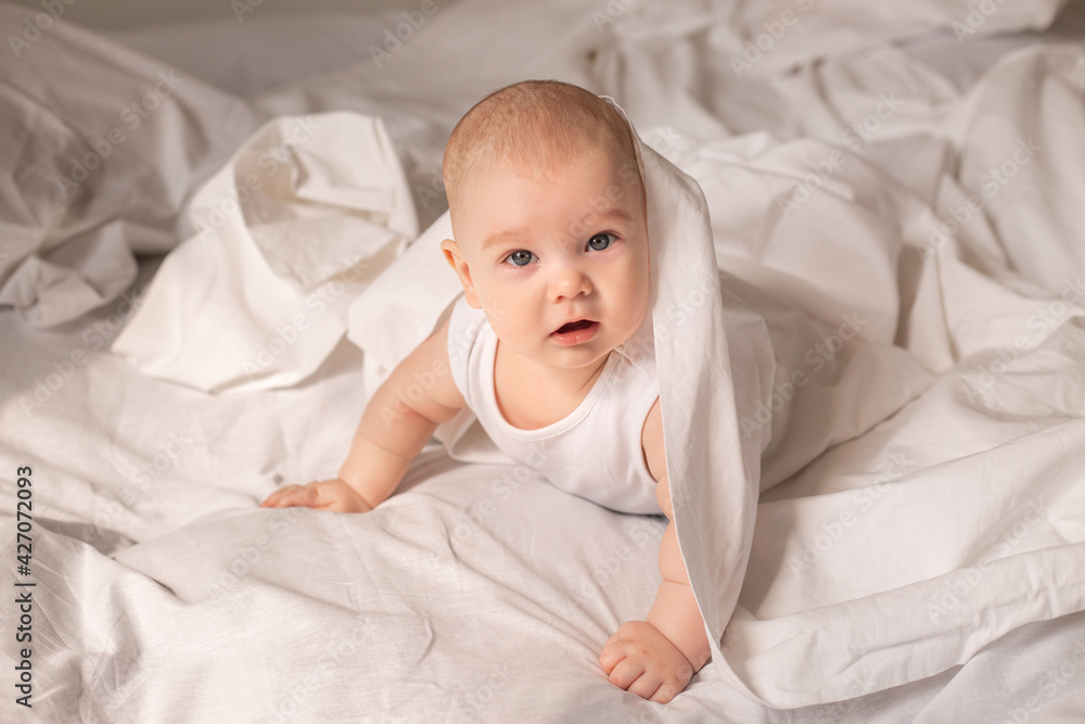 Cute toddler in white bodysuit lies in bed with white bedding Cute toddler in white bodysuit lies in bed with white bedding