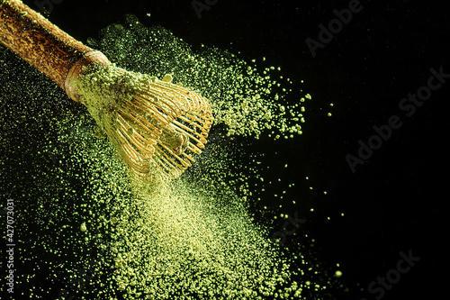 Photos Bamboo whisk with flying matcha tea powder on a black background.