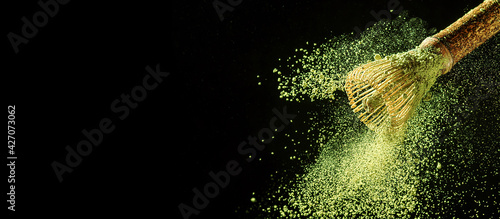 Bamboo whisk with flying matcha tea powder on black background with copy space. photo