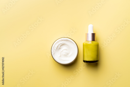 Set of natural cosmetics for face care serum bottle and cream on yellow background, top view