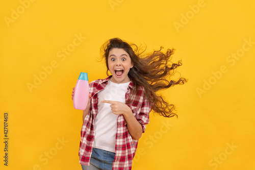 happy teen girl with long curly hair hold shampoo bottle, hairdresser