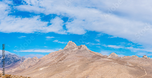 Light brown barren desert mountain peaks under a blue sky white white clouds.