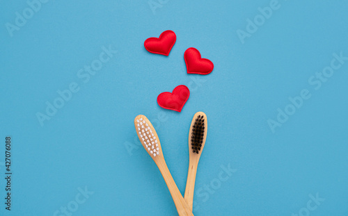 Two bamboo toothbrushes with a red heart on a blue background with copy space. Valentine's Day. Love. Bamboo, eco-friendly, waste-free and plastic-free toothbrushes. Top view, flat lay. copy space
