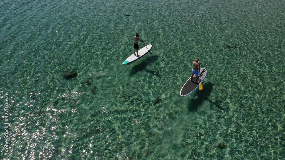 Aerial drone view of friend athletes exercising sup board or Stand Up Paddle board in emerald exotic shallow bay