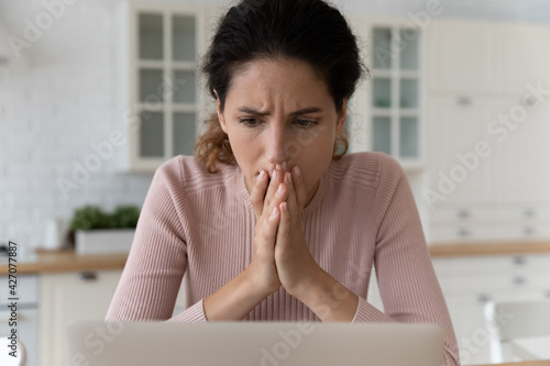 Shocked hispanic female read unexpected bad news on pc screen feel panic anxiety. Scared young latina woman overwhelmed with blackmail scam message stack palms by face pray to see way out of problem