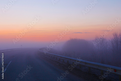 A bright dawn in pastel colors and with heavy fog greets us on a country road.
