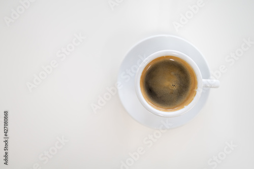 Top view of white cup of hot black coffee (Americano) with plate on white desk with copy space.