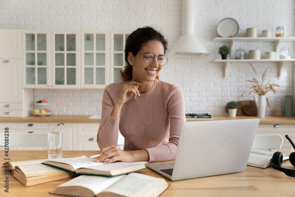 Smiling young latin lady learn remotely from home look on laptop screen distracted from reading paper literature. Positive woman student do academic research study printed books using online library Smiling young latin lady learn remotely from home look on laptop screen distracted from reading paper literature. Positive woman student do academic research study printed books using online library