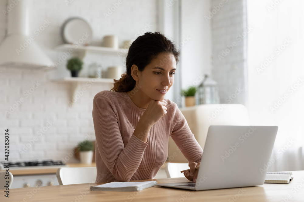 Web lecture. Focused young latina female sit at kitchen table look at pc screen listen to teacher think on problem to solve. Attentive lady remote student learn from home watch webinar training online Web lecture. Focused young latina female sit at kitchen table look at pc screen listen to teacher think on problem to solve. Attentive lady remote student learn from home watch webinar training online