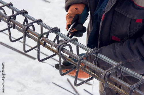 Concrete reinforcement. Tool at a construction site. The construction tool for monolithic works. Workers hands using steel wire and pincers to secure rebar