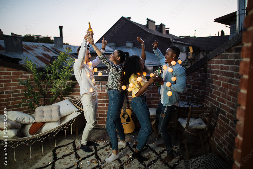 Full length portrait of joyful friends relaxing with alcoholic drinks and favorite music on party. Concept of relaxation, multiethnicity and carefree.