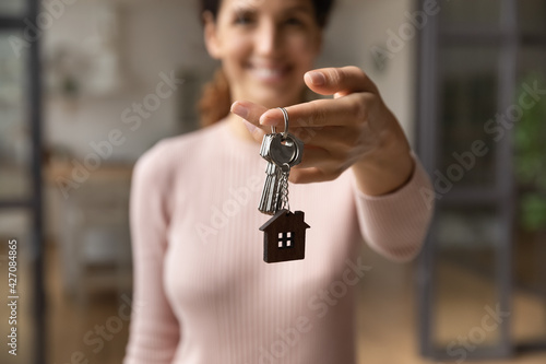 Please take your keys. Close up blurred portrait of smiling young latin lady real estate owner seller propose you client to get key from new home flat. Focus on female broker hand giving bunch of keys photo