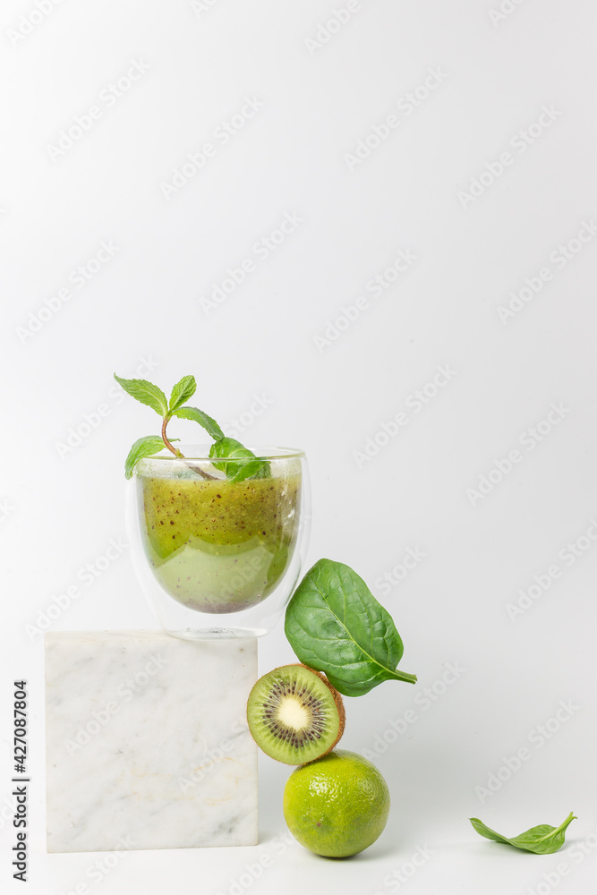 Fototapeta premium The concept of a detox cocktail of fruits and vegetables. Smoothie with kiwi, mint, lime and spinach on a stand over a white background. Vertically, copy space