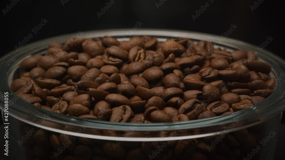 Slow optical zoom out from a glass plate filled with aromatic roasted coffee beans in a dark black room Slow optical zoom out from a glass plate filled with aromatic roasted coffee beans in a dark black room