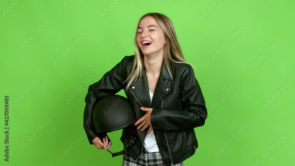 Young woman holding a motorcycle helmet smiling a lot while covering mouth over isolated background on green screen chroma key Young woman holding a motorcycle helmet smiling a lot while covering mouth over isolated background on green screen chroma key