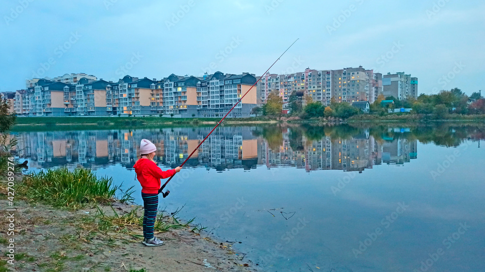 girl fishing on river overlooking large residential area. City landscape