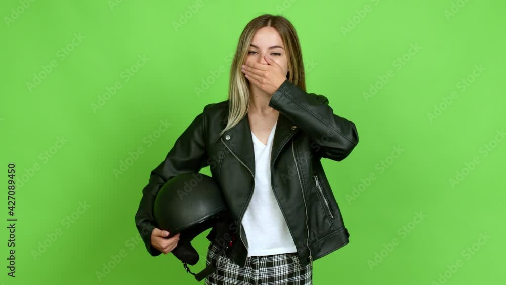 Young woman holding a motorcycle helmet covering mouth with hands. Can not speak over isolated background on green screen chroma key Young woman holding a motorcycle helmet covering mouth with hands. Can not speak over isolated background on green screen chroma key