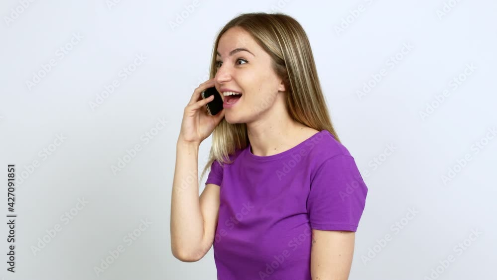 Young woman talking on mobile phone shouting to the lateral and announcing something over isolated background Young woman talking on mobile phone shouting to the lateral and announcing something over isolated background