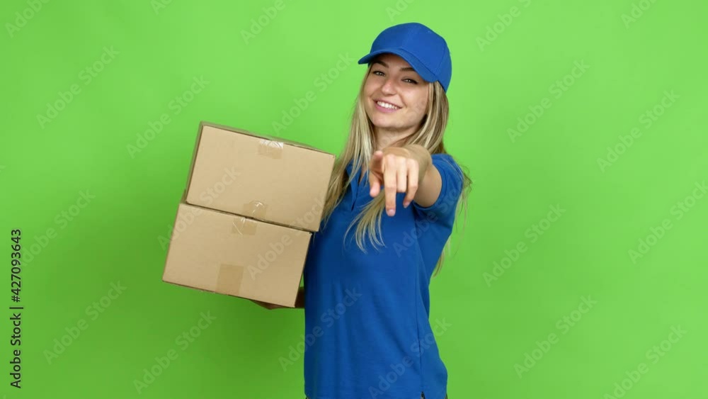 Young woman holding boxes for delivery points finger at you with a confident expression over isolated background on green screen chroma key Young woman holding boxes for delivery points finger at you with a confident expression over isolated background on green screen chroma key