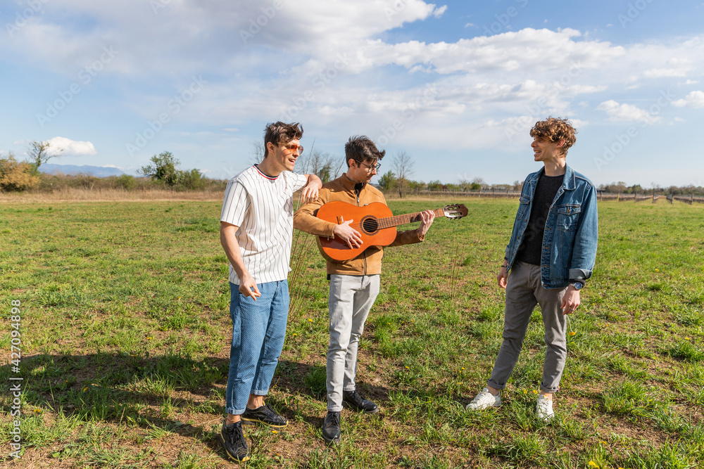 three friends in a field meet to sing and play guitar cheerfully together